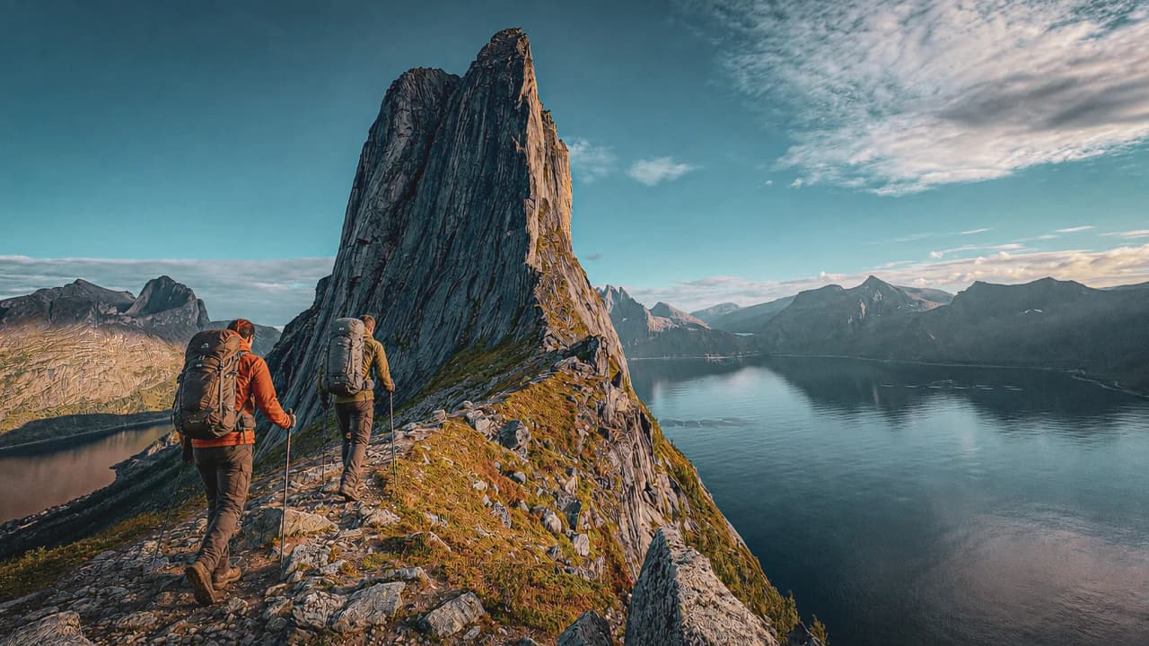 Wandelen op het eiland Senja, met majestueuze bergtoppen en een rustige fjord op de achtergrond.