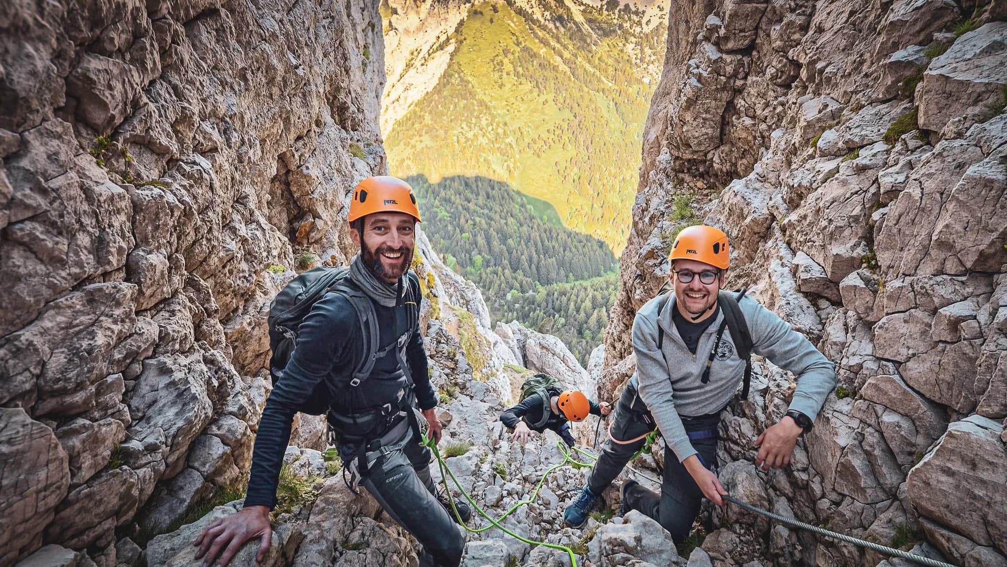Three smiling climbers in a rock crack, surrounded by lush green countryside.