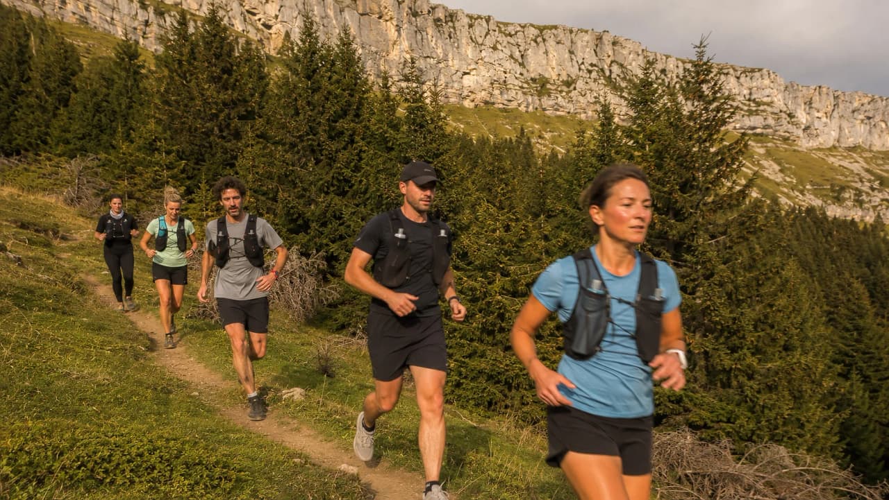 Groupe de randonneurs sur un sentier alpin, entouré de forêts et de falaises majestueuses.