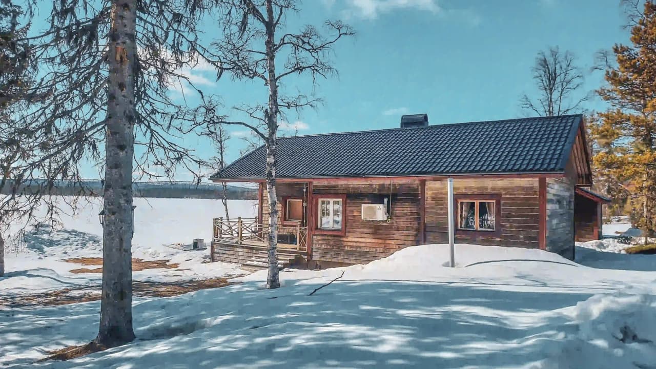 Wooden chalet on the edge of a frozen lake, surrounded by brilliant snow and Lapland landscapes.