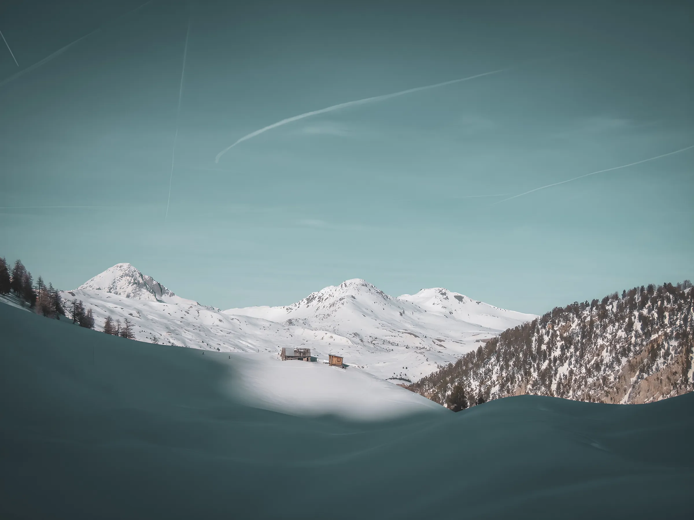 Snow-capped alpine scenery with majestic mountains and a picturesque Mountain hut under a blue sky.