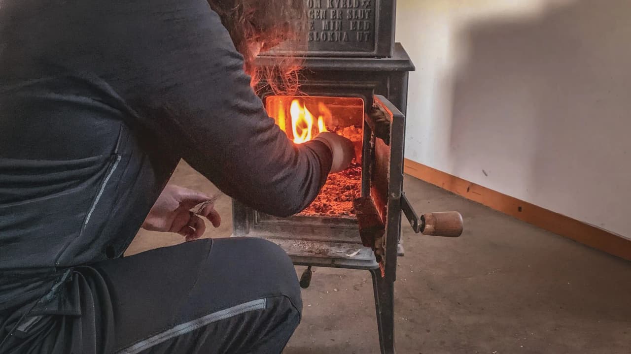 Personne ajoutant du bois à un poêle, créant une ambiance chaleureuse en montagne.