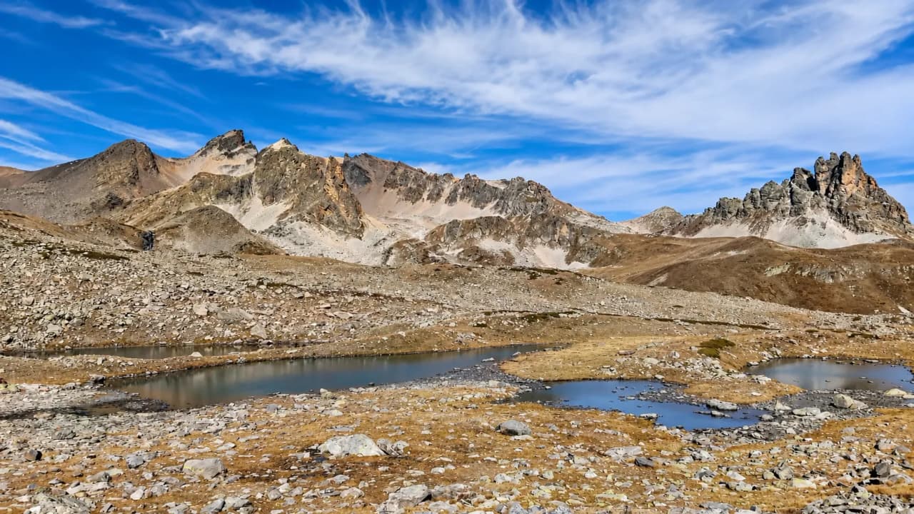 Vaste paysage alpin avec lacs scintillants, montagnes majestueuses et ciel bleu éclatant.