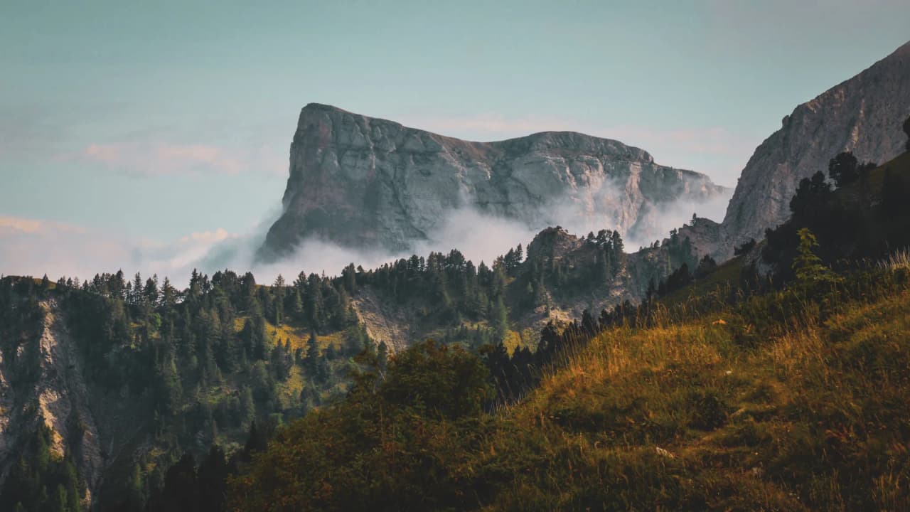 Majestic mountains under a blue sky, shrouded in mist and soothing greenery.