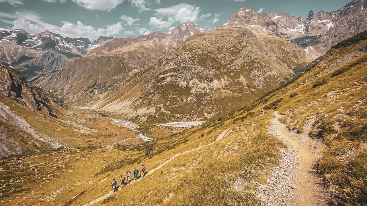Randonneurs progressant sur un sentier montagneux, entourés de sommets majestueux et de vallées.