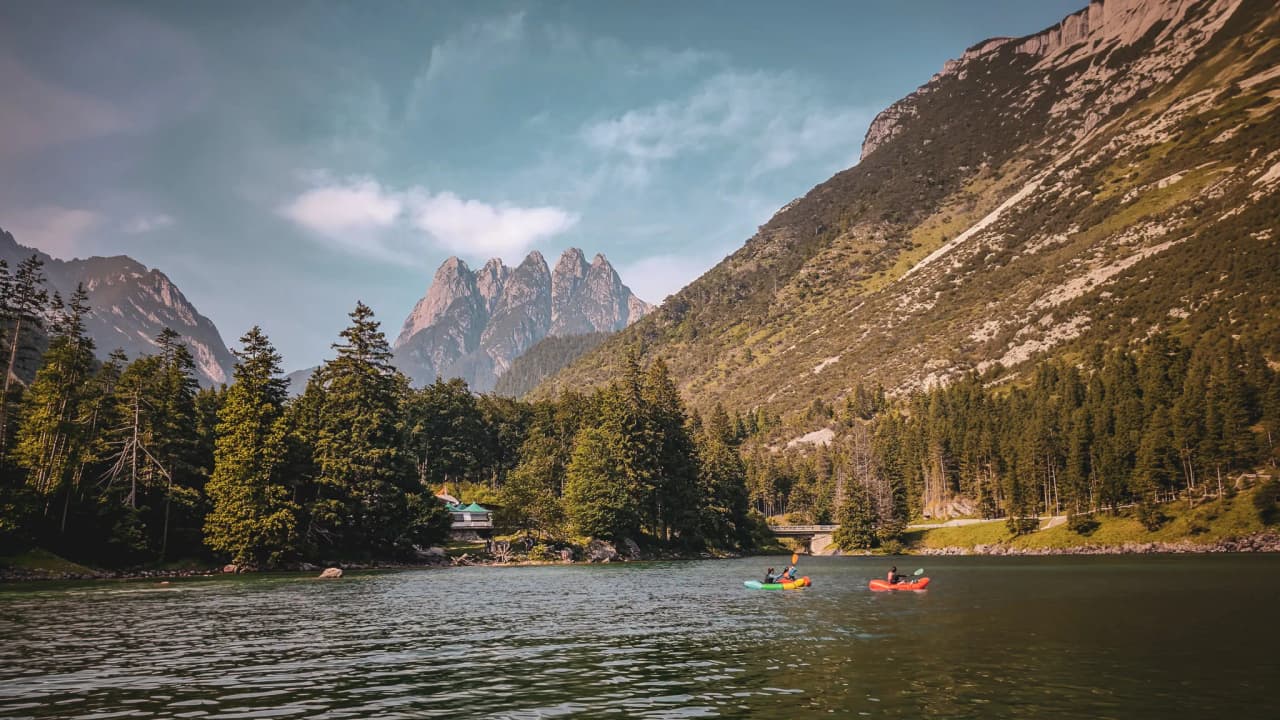 Two kayakers explore calm waters surrounded by majestic mountains in Slovenia.