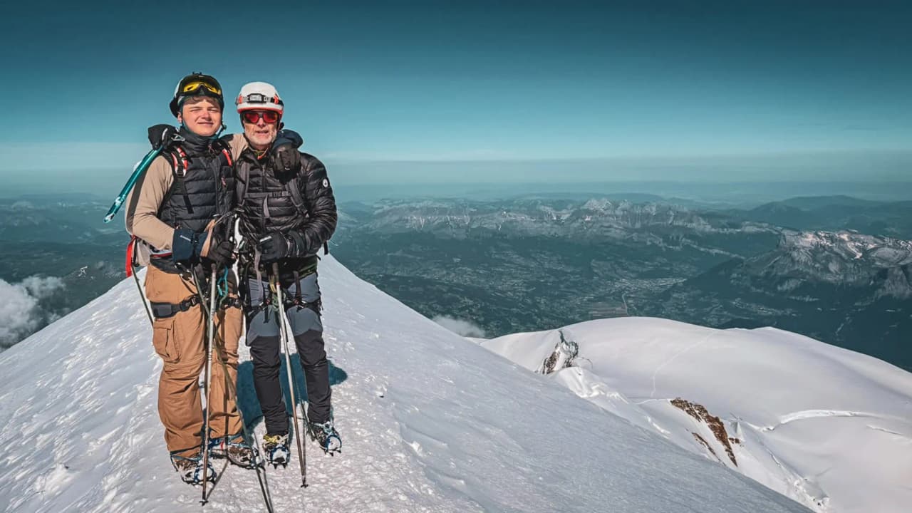 Two mountaineers on the summit of Mont Blanc, surrounded by majestic, snow-covered landscapes.