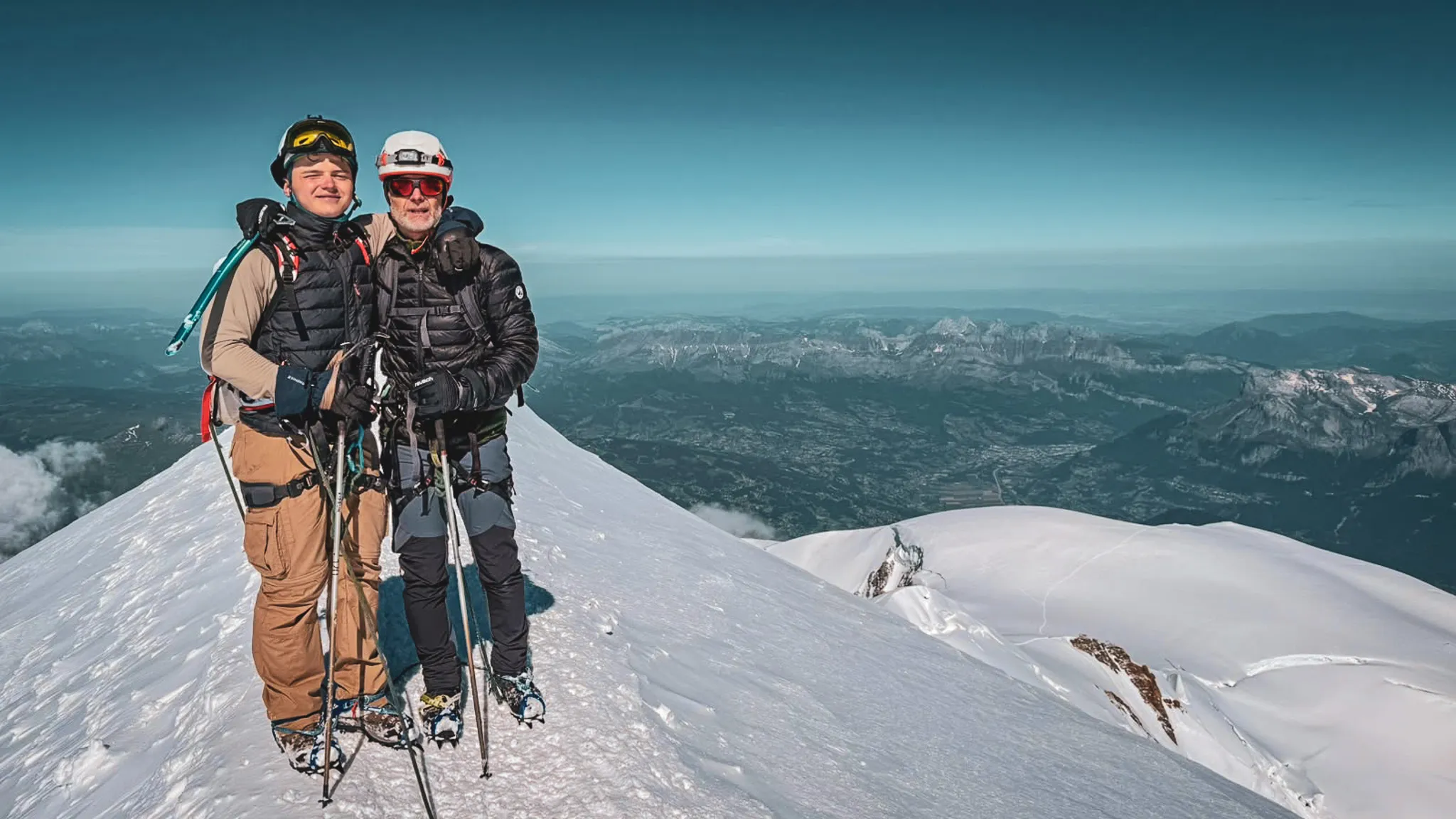 Deux alpinistes au sommet du Mont Blanc, entourés de paysages majestueux et enneigés.