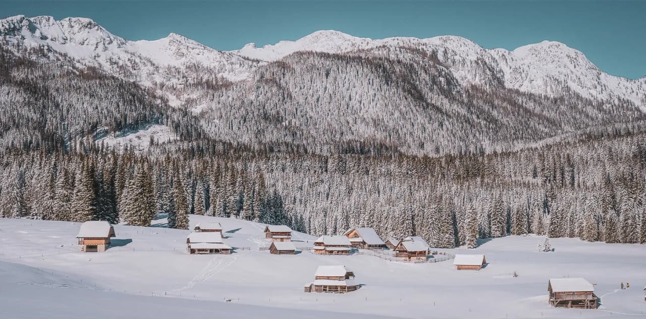 Paysage enchanteur des Alpes juliennes en hiver, avec des chalets enneigés et des forêts majestueuses.