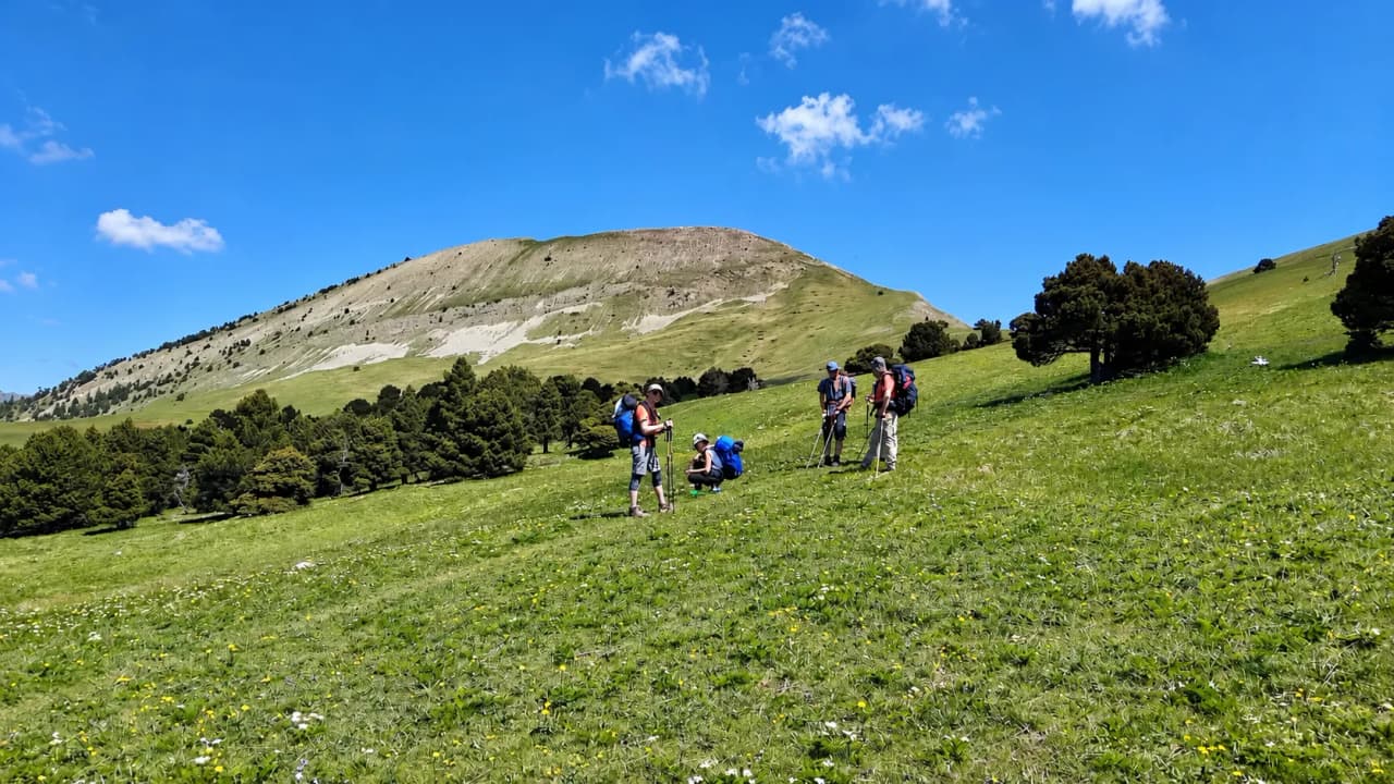 Een groep wandelaars op een groene vlakte, met een stralend blauwe lucht en bergen op de achtergrond.