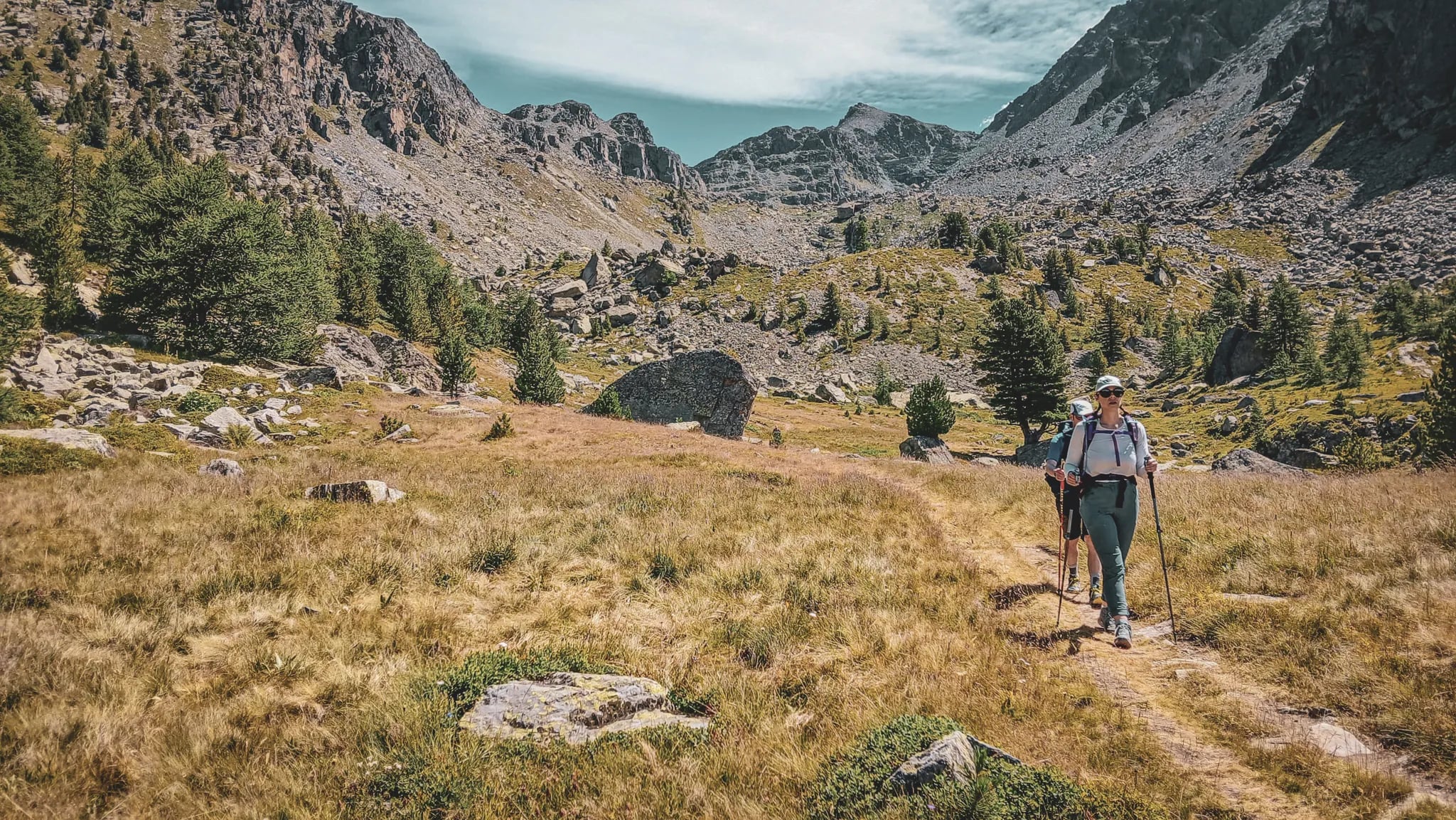 Un randonneur sur sentier alpin, entouré de paysages sauvages et de montagnes majestueuses.