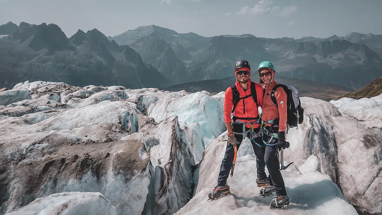 Couple souriant sur un glacier à Chamonix, avec des montagnes majestueuses en arrière-plan.