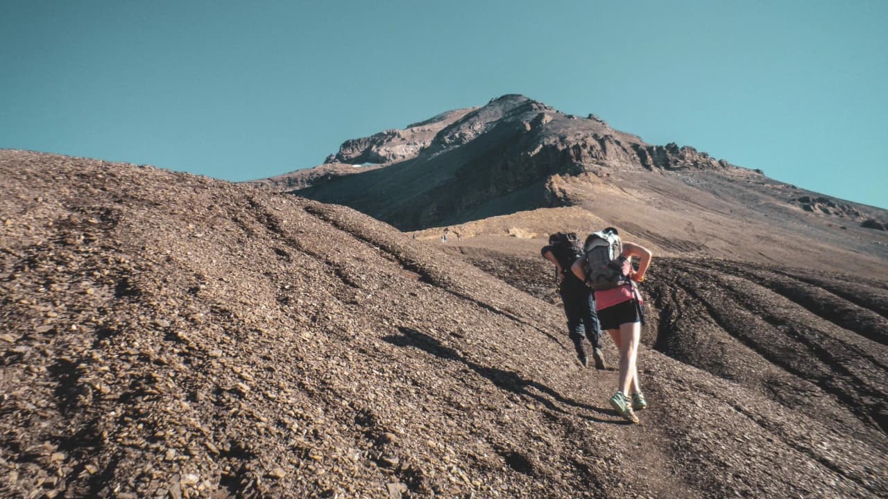 Hikers climbing an alpine trail, with a breathtaking mountain landscape in the background.