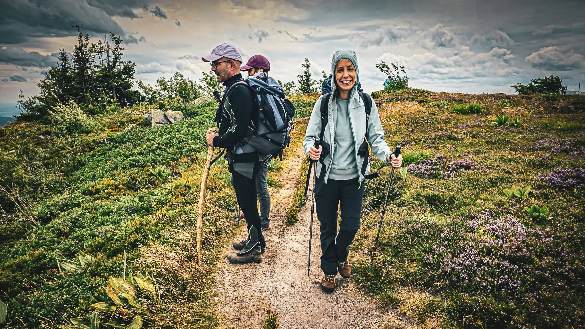 Trois randonneurs souriants sur un sentier verdoyant des Vosges, entourés de nature et d’émerveillement.