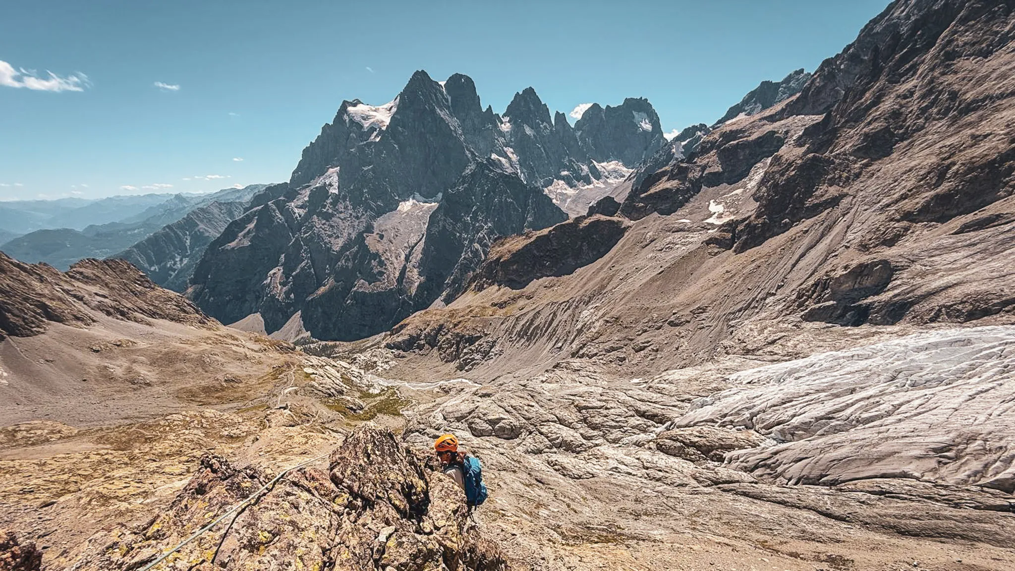 Un alpiniste grimpe une montagne majestueuse dans les Écrins, sous un ciel dégagé et ensoleillé.