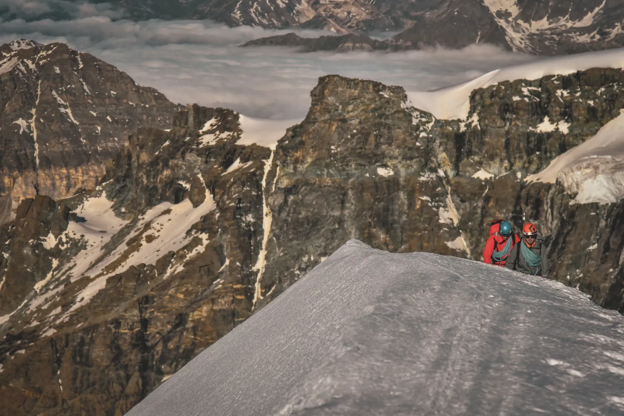 Alpinistes sur un sommet enneigé, avec des montagnes majestueuses en arrière-plan.
