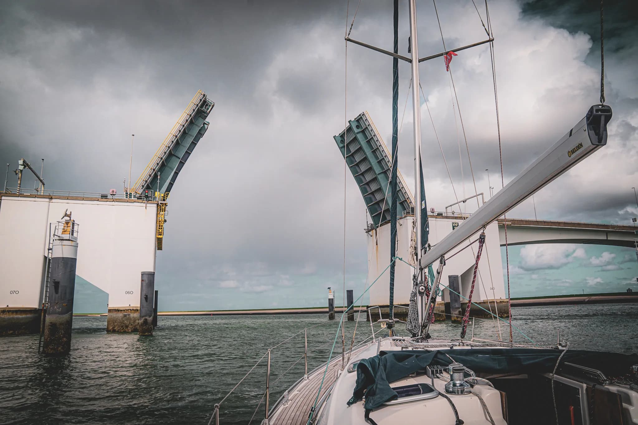 Voilier naviguant sous un pont levant, ciel nuageux, ambiance maritime captivante.
