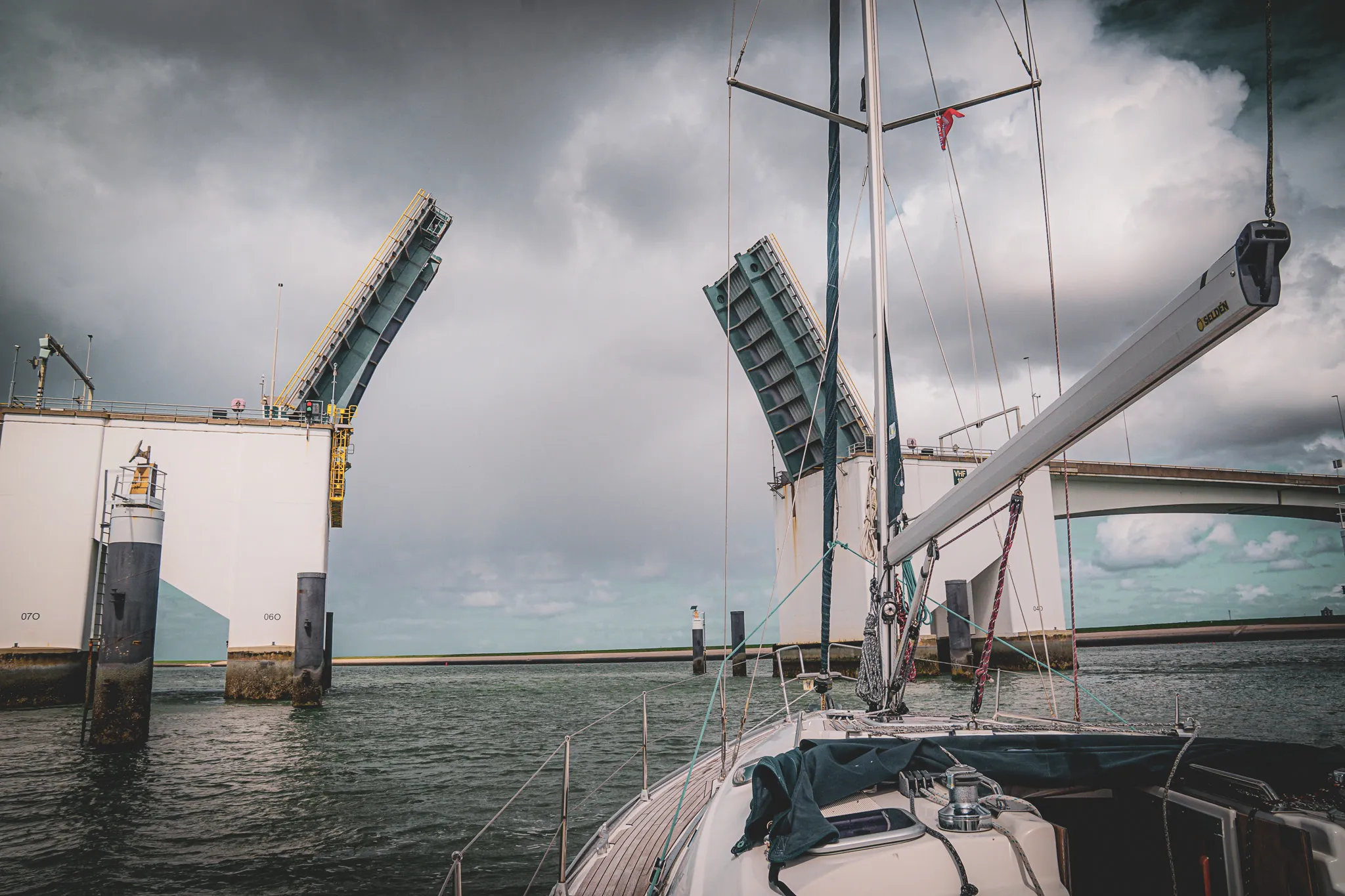 Voilier naviguant sous un pont levant, ciel nuageux, ambiance maritime captivante.