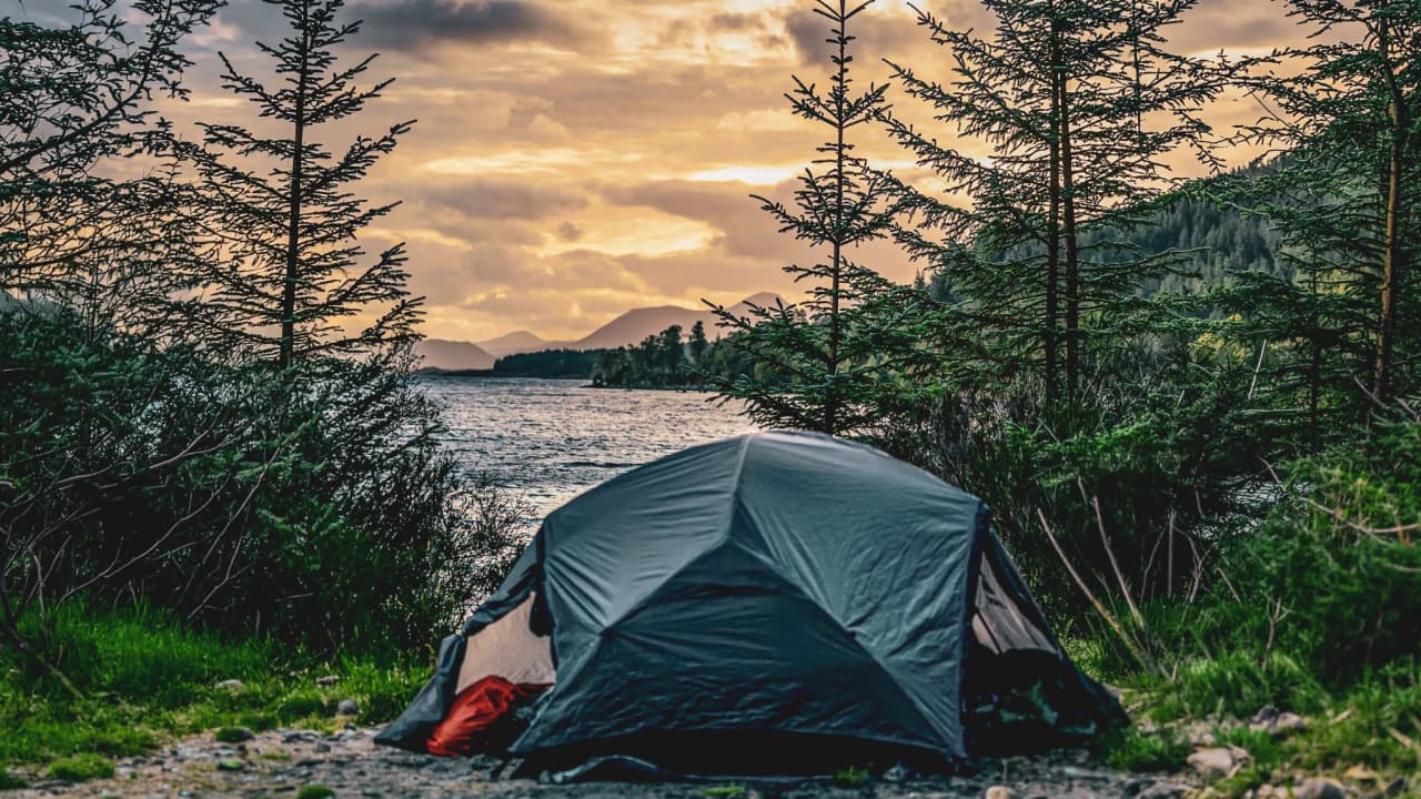 Tent aan de rand van een loch, bergen op de achtergrond onder een gouden hemel, een uitnodiging voor Schots avontuur.