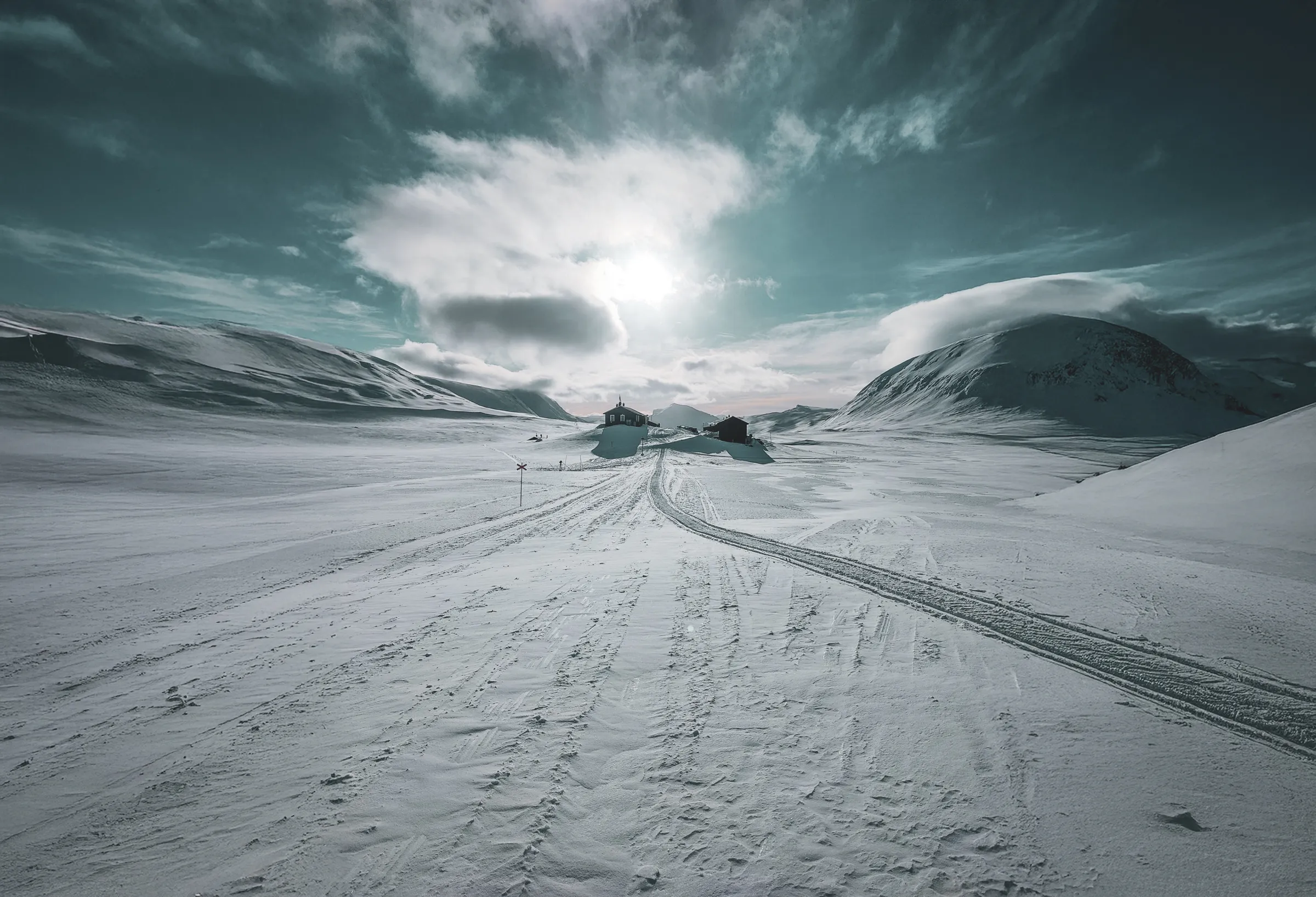 paysage enneigé sous un ciel dramatique, avec des montagnes et des cabanes isolées.