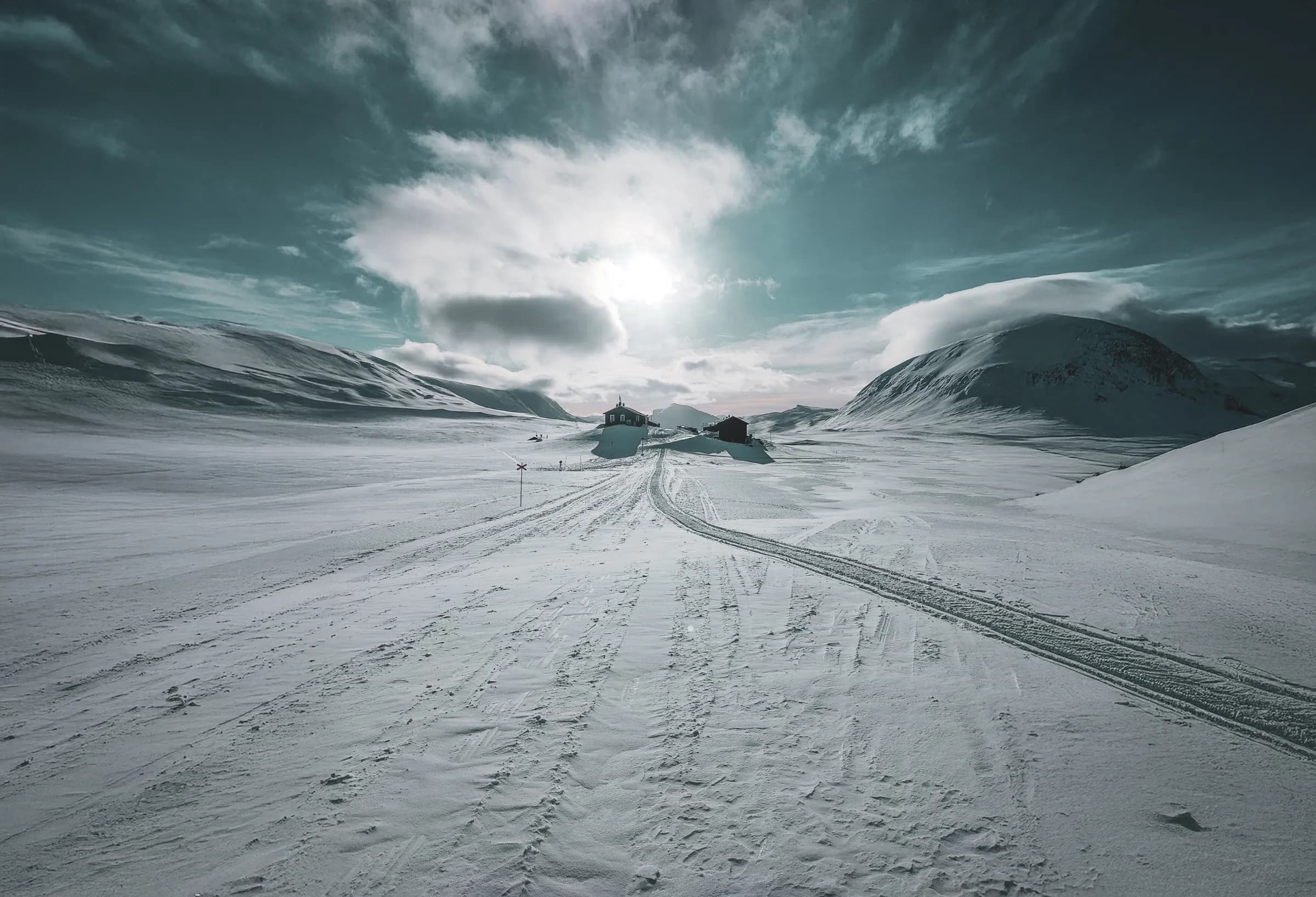 snowy landscape under a dramatic sky, with mountains and isolated cabins.