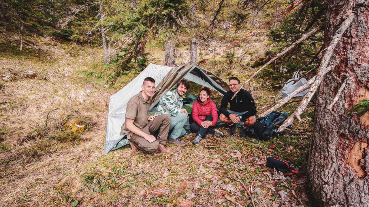 Un groupe de quatre personnes souriantes sous un abri en pleine nature, prêt pour l'aventure.