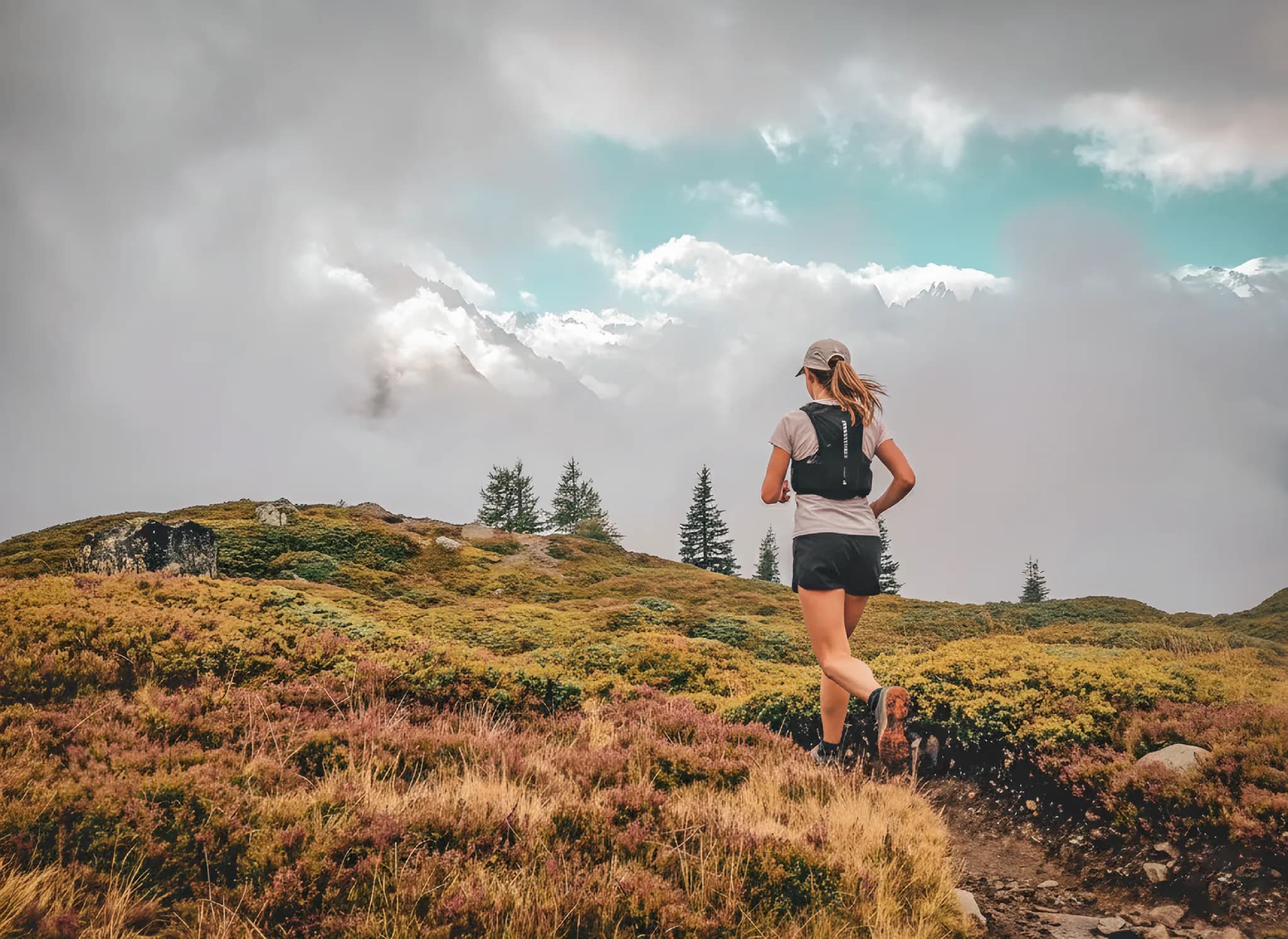 Vrouw rent op een alpenpad, omringd door berglandschappen en indrukwekkende wolken.