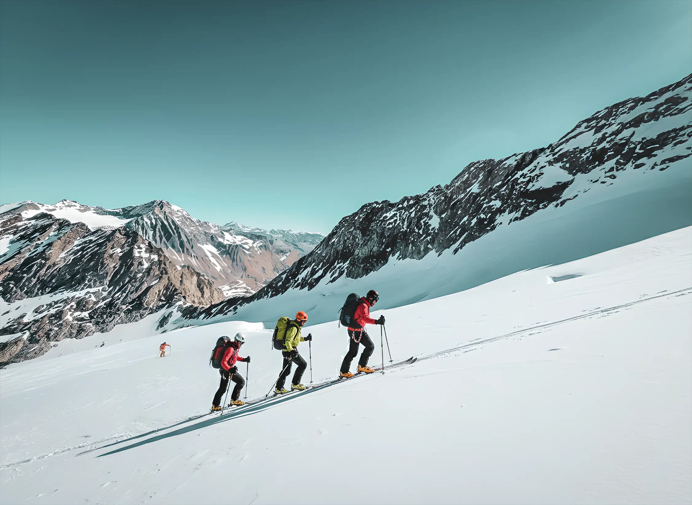 Three ski tourers climb a glacier, with spectacular mountain scenery in the background.