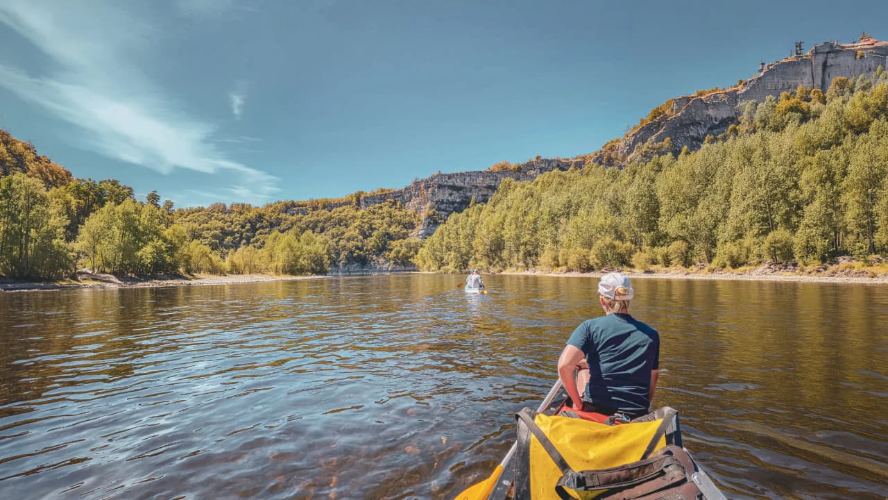 Canoë sur la Dordogne, paysage paisible avec châteaux et forêts verdoyantes au soleil.