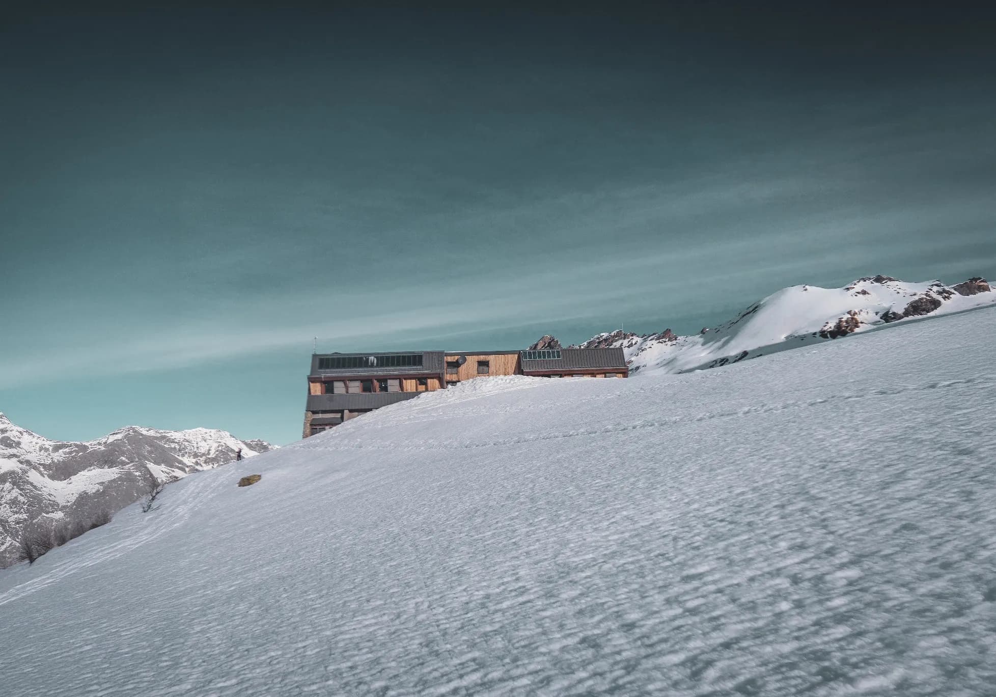Refuge montagnard isolé, enneigé, sous un ciel bleu clair, offrant une vue sur les sommets alpins.