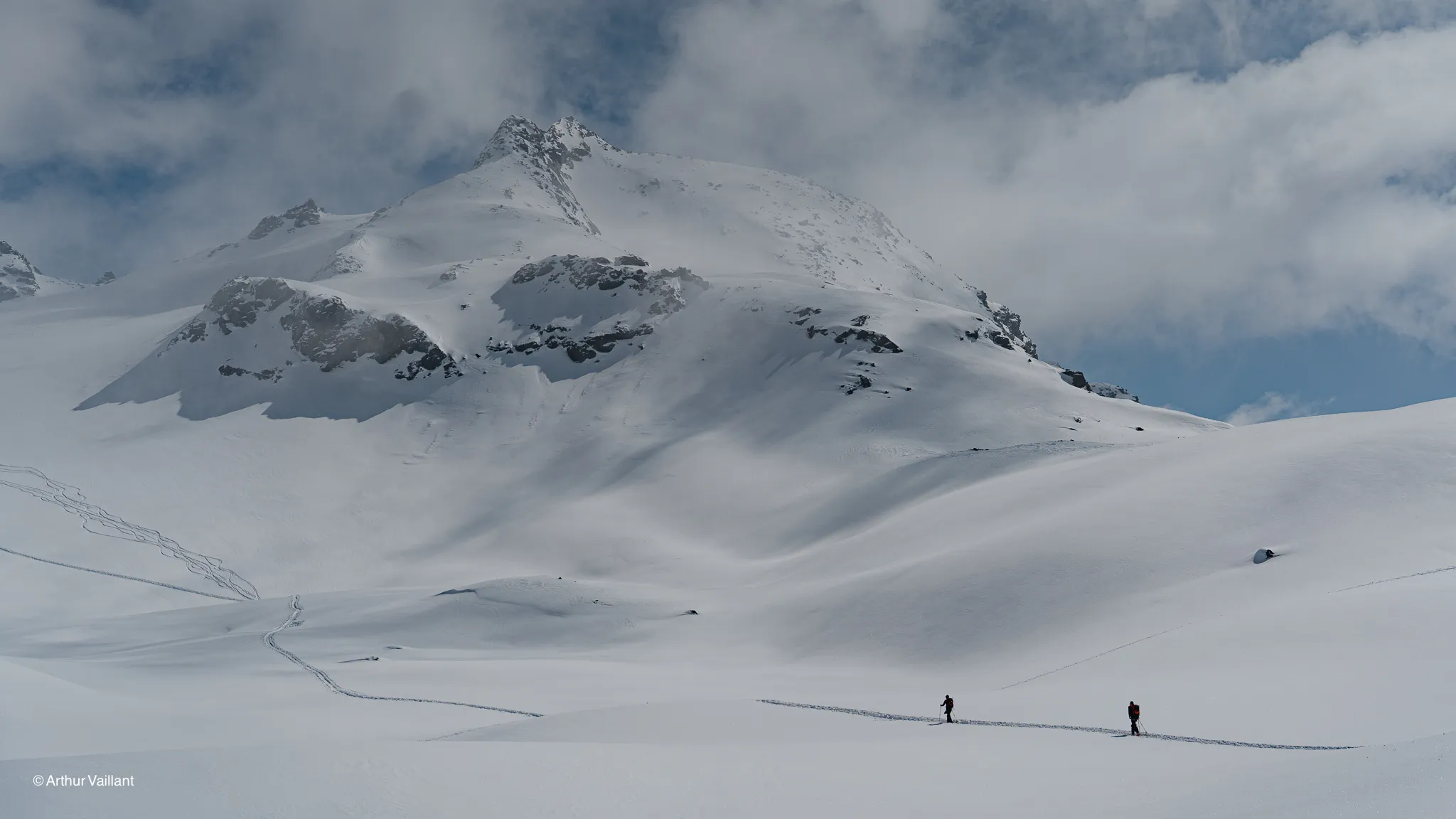 Skiers are making their way across a snow-covered alpine landscape, surrounded by majestic peaks.