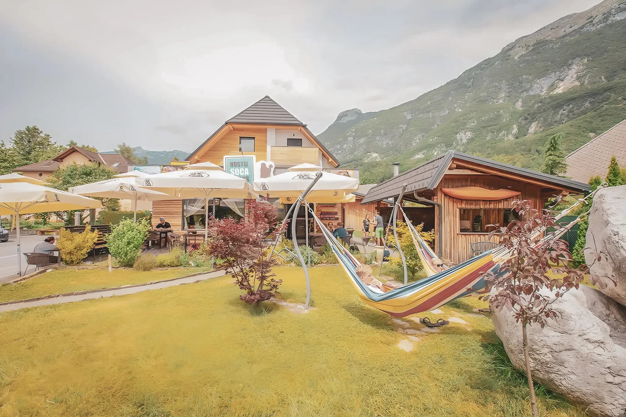 Un jardin vibrant avec hamacs colorés, devant un charmant hostel alpin en Slovénie.