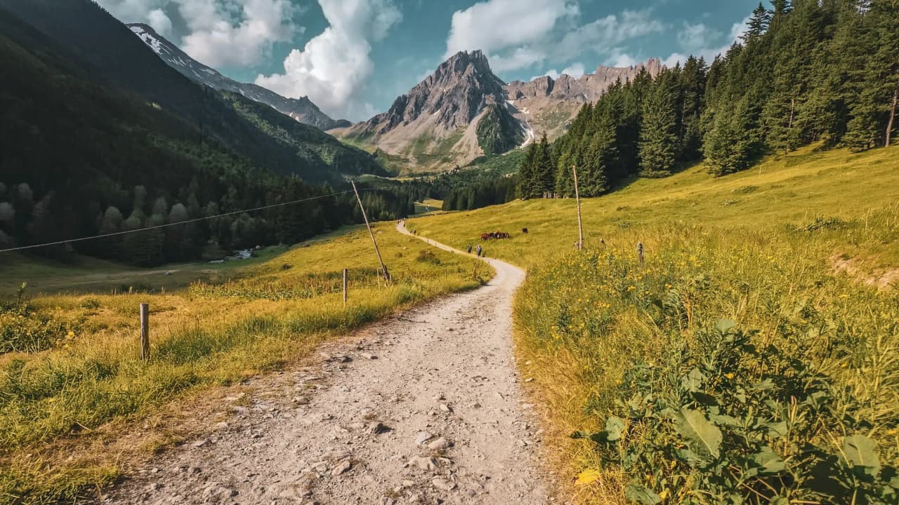 A path winding through lush green countryside, surrounded by majestic mountains.