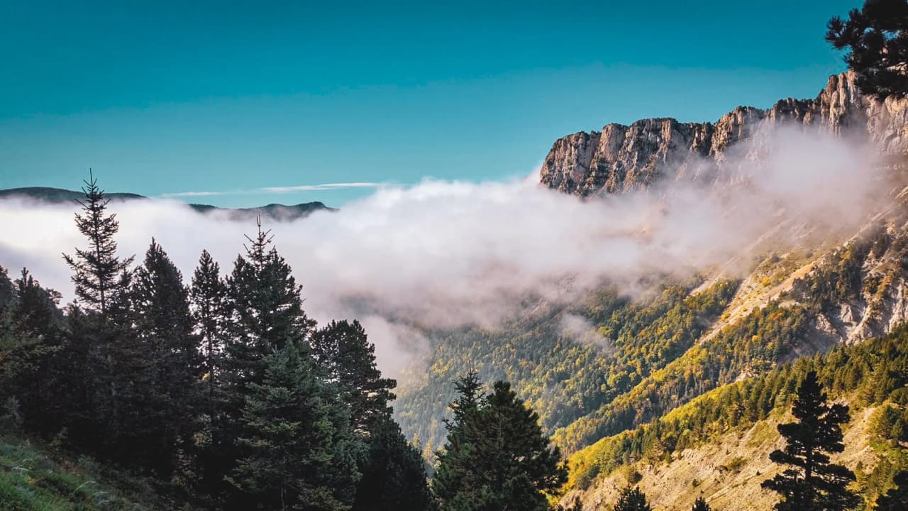 Spectaculair panorama van de Mont Aiguille, met wolken die flirten met de toppen en weelderige bossen.