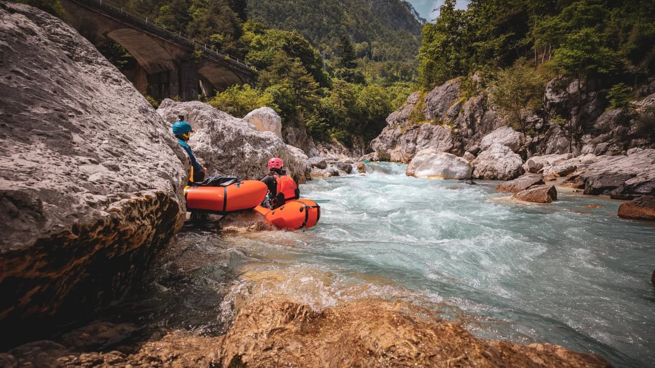 Two packraft adventurers explore a crystal-clear river, surrounded by majestic Alpine scenery.