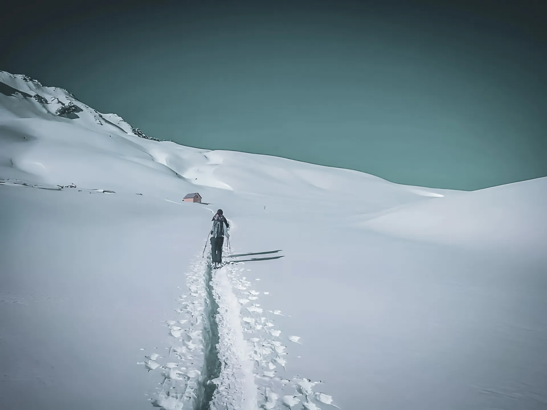 A hiker crosses snow-covered landscapes, facing majestic peaks and a cosy Mountain hut.