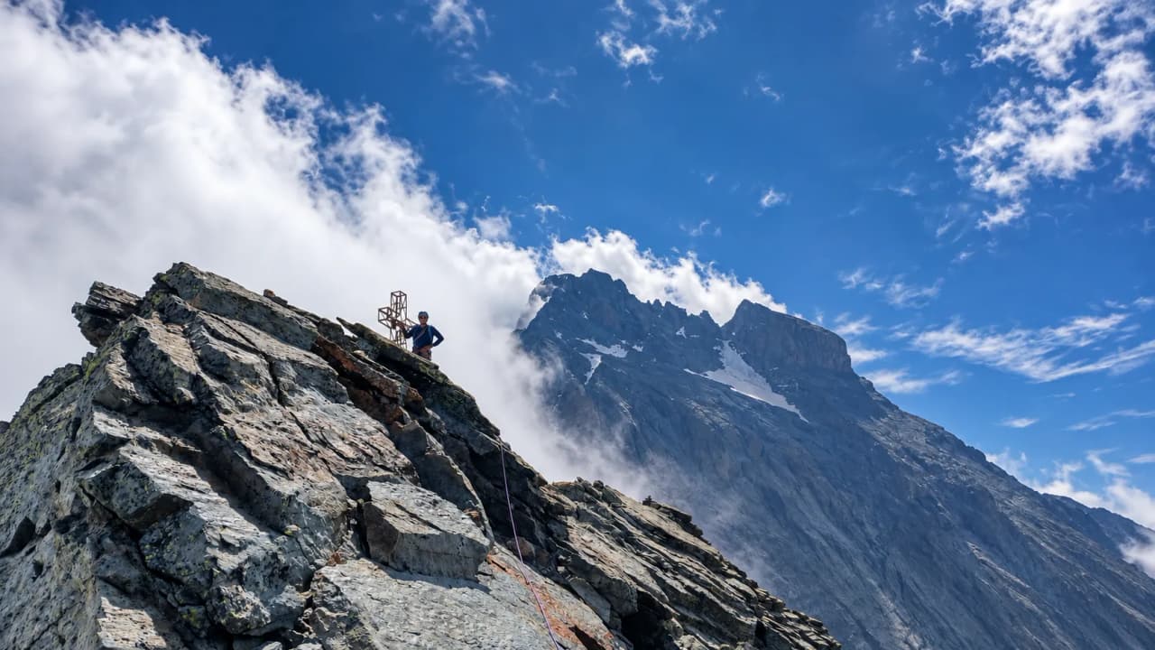 The majestic Monte Viso against a blue sky; a mountaineer reaches the summit, ready for adventure.
