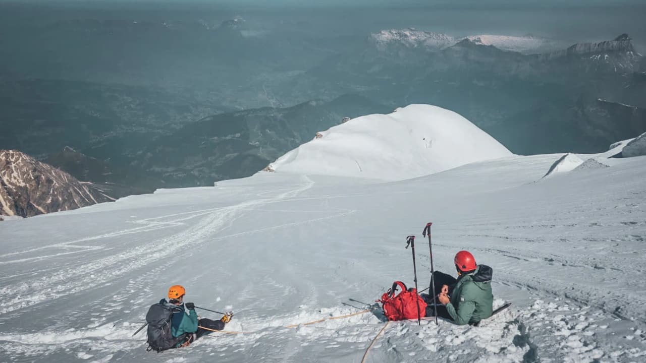 Drie klimmers liggen op de sneeuw en kijken uit over de Mont Blanc en zijn majestueuze landschappen.