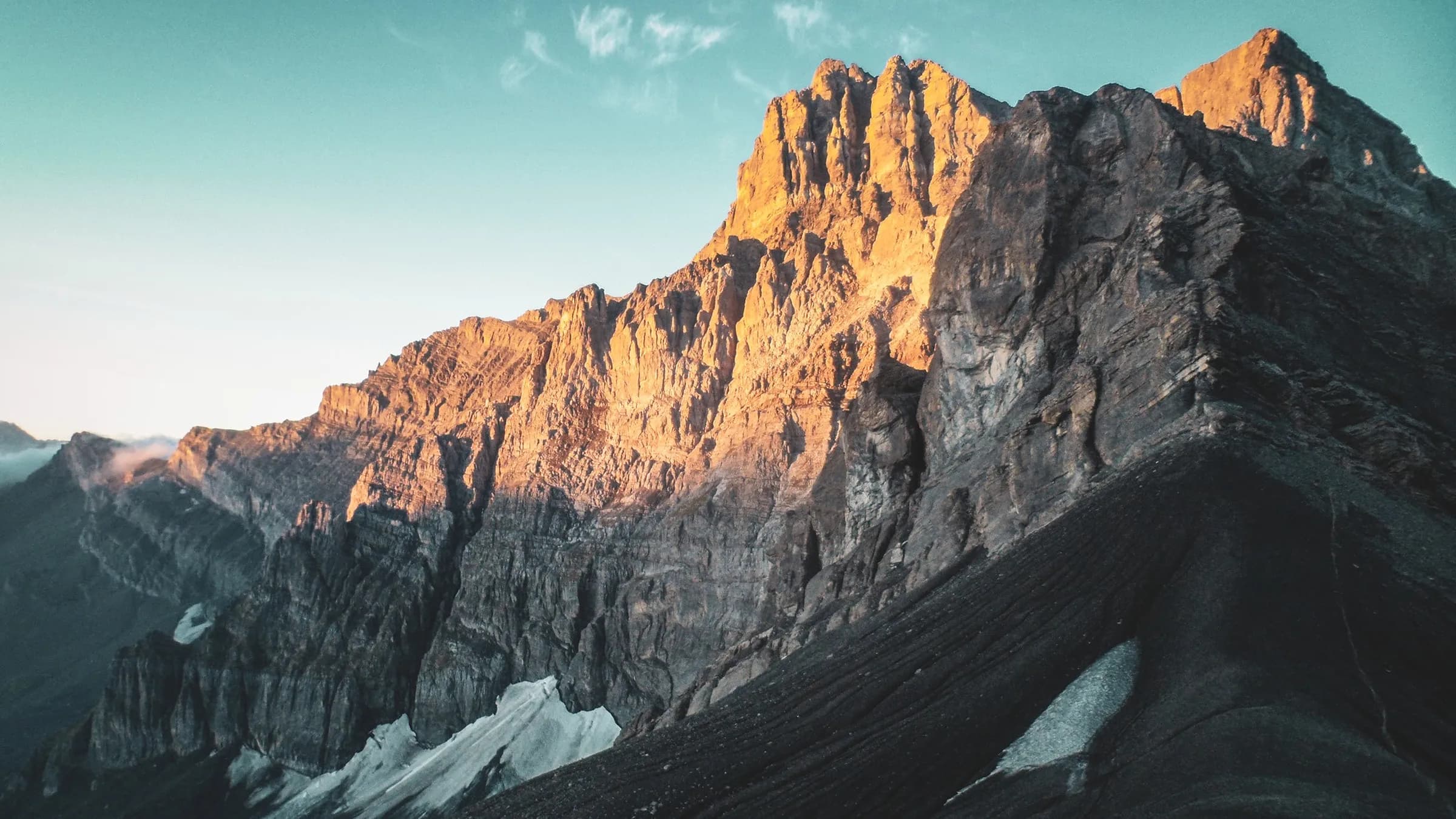Montagnes majestueuses aux crêtes dorées, sous un ciel azur, invitation à l'aventure alpine.