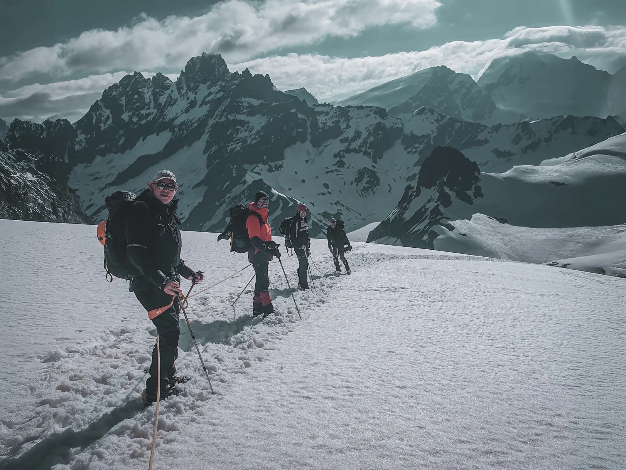 A team of mountain hikers on a glacier with majestic peaks in the background.