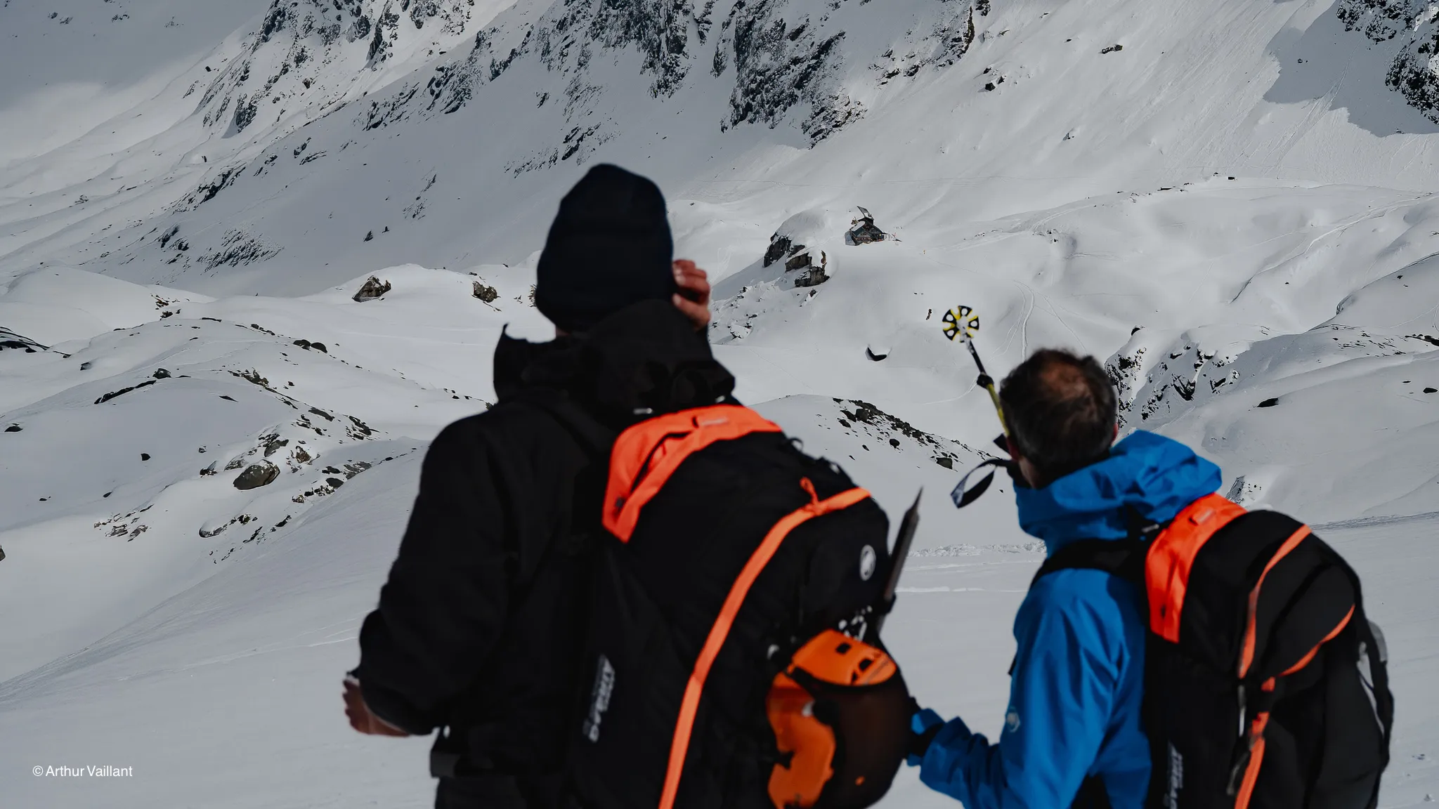 Two skiers are admiring the majestic snow-capped peaks, ready to embark on an alpine adventure.