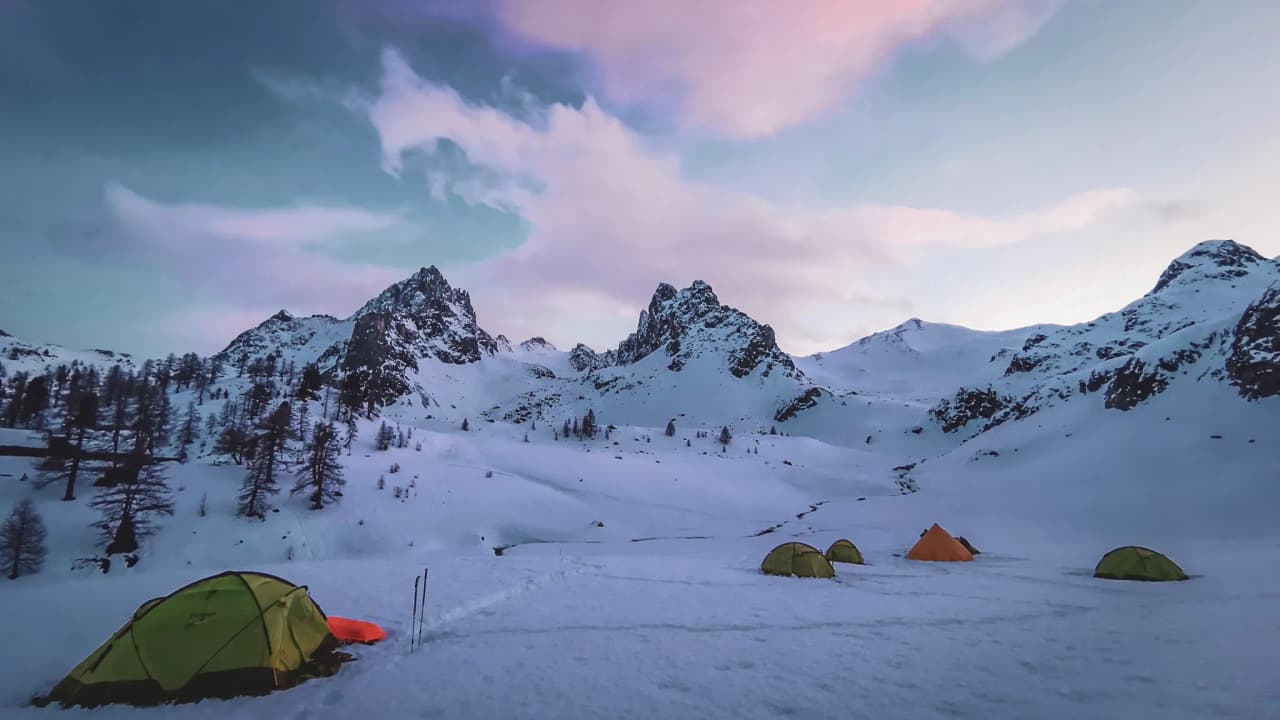 A winter camp in the heart of the Cerces, with colourful tents set against a majestic snowy landscape.