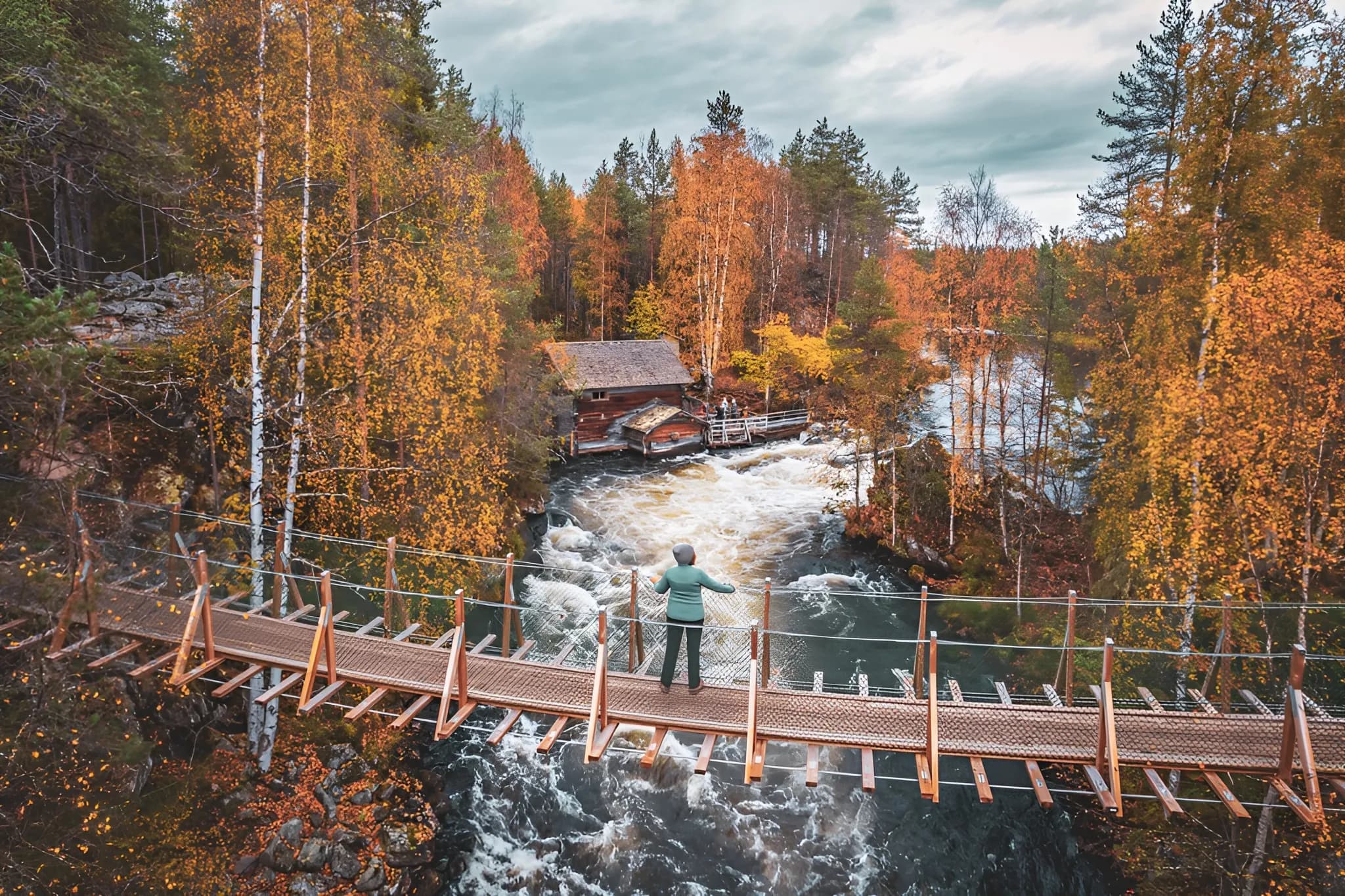 Suspension bridge over a tumultuous river, surrounded by autumn-coloured trees.