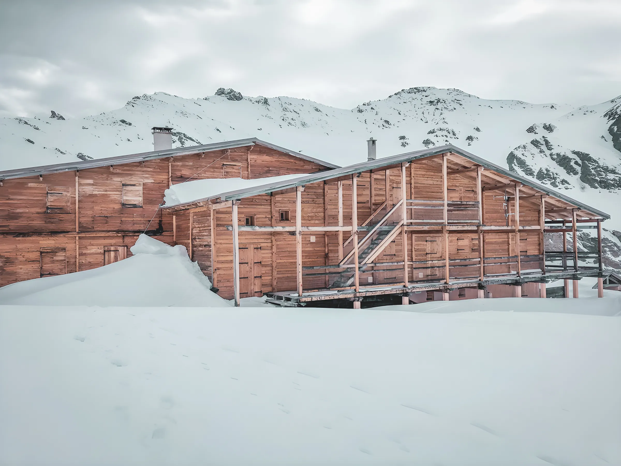 A snow-covered wooden Mountain hut surrounded by majestic mountains, ideal for ski touring adventures.