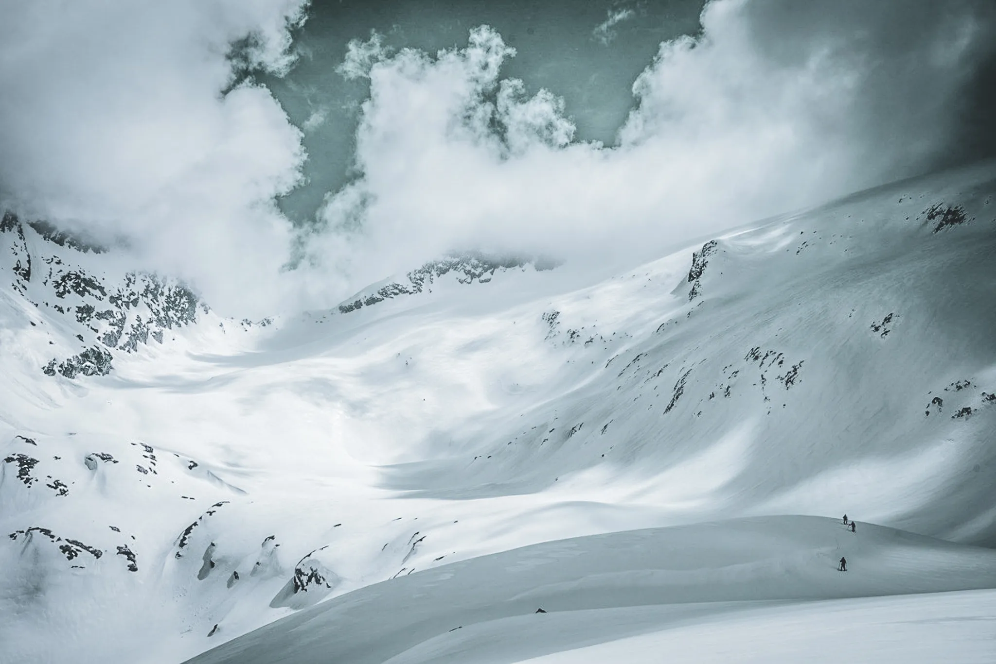 A majestic Alpine landscape, with skiers on immaculate glaciers under cloudy skies.