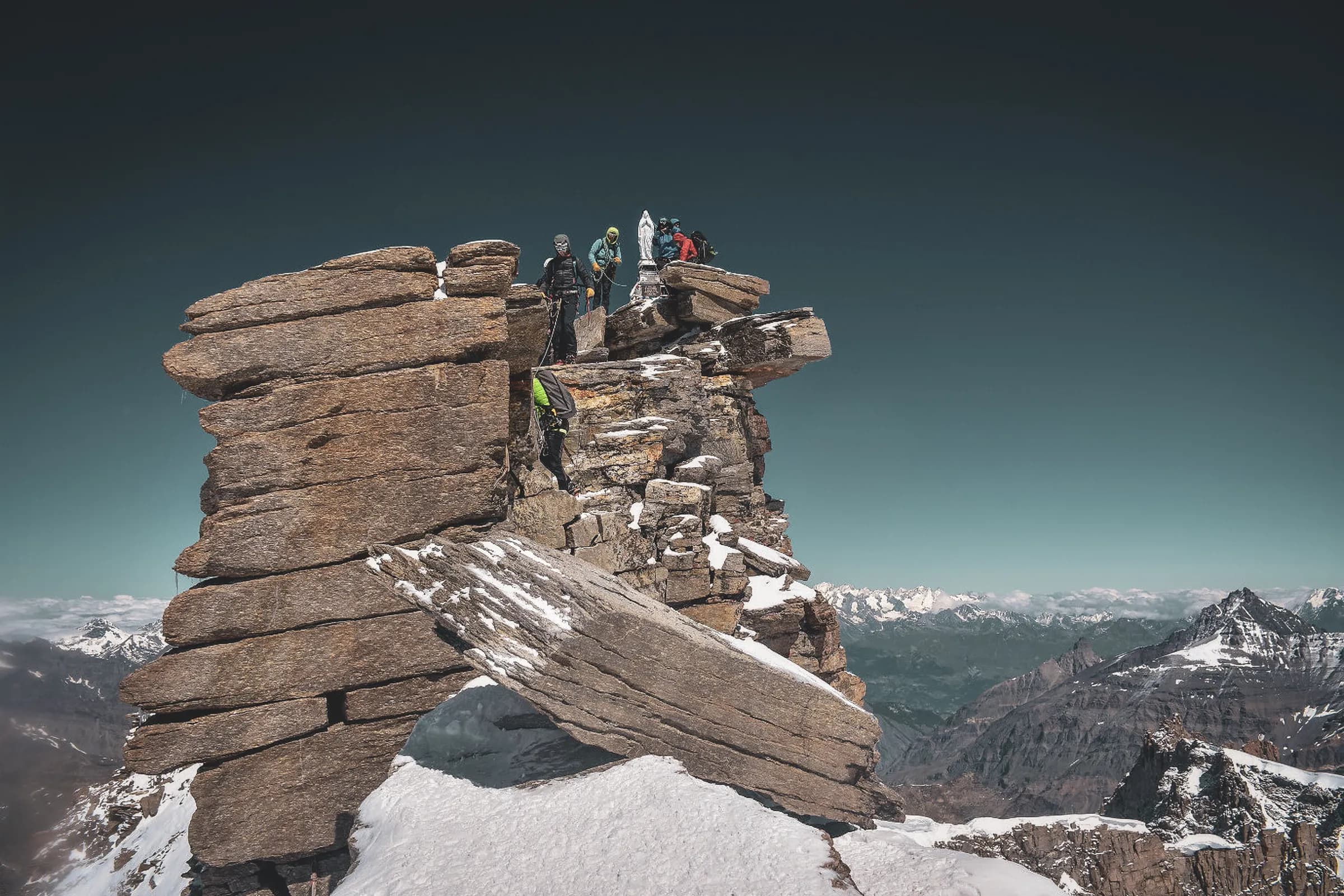 A group of climbers on a spectacular summit, overlooking snow-capped mountains. Breathtaking!