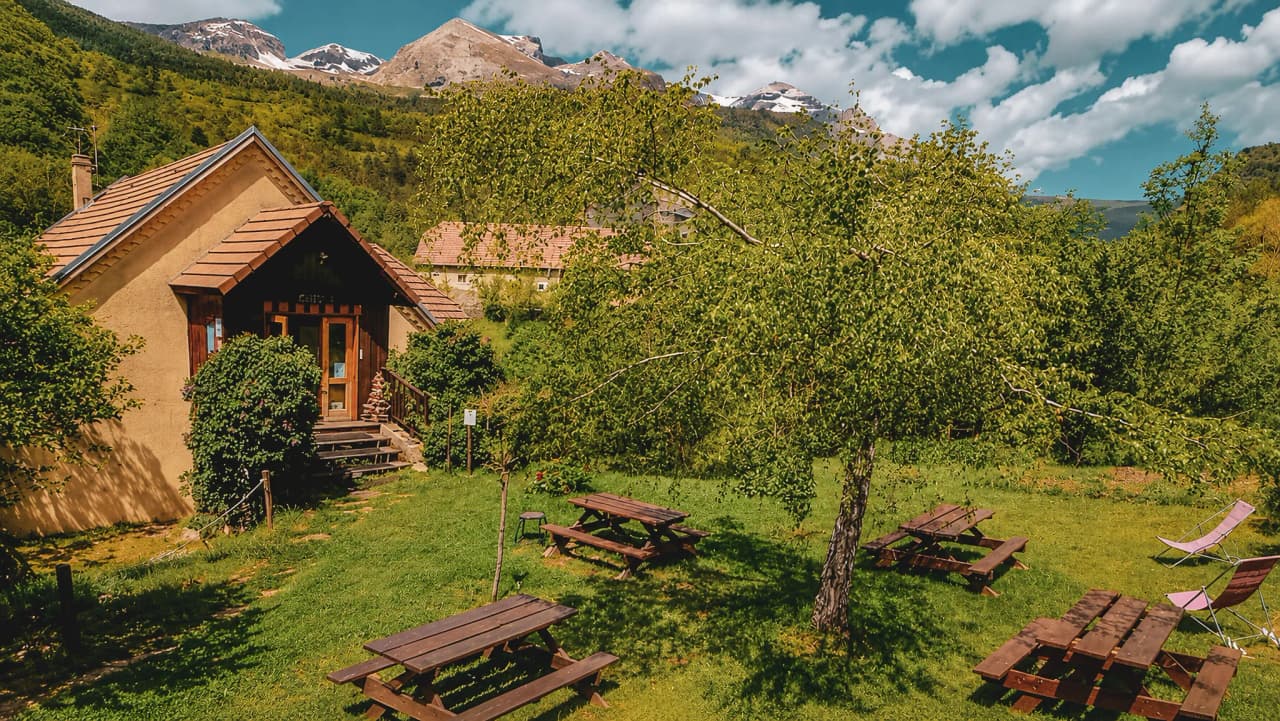 Charmante houten hut omgeven door groen, met majestueuze bergen op de achtergrond.