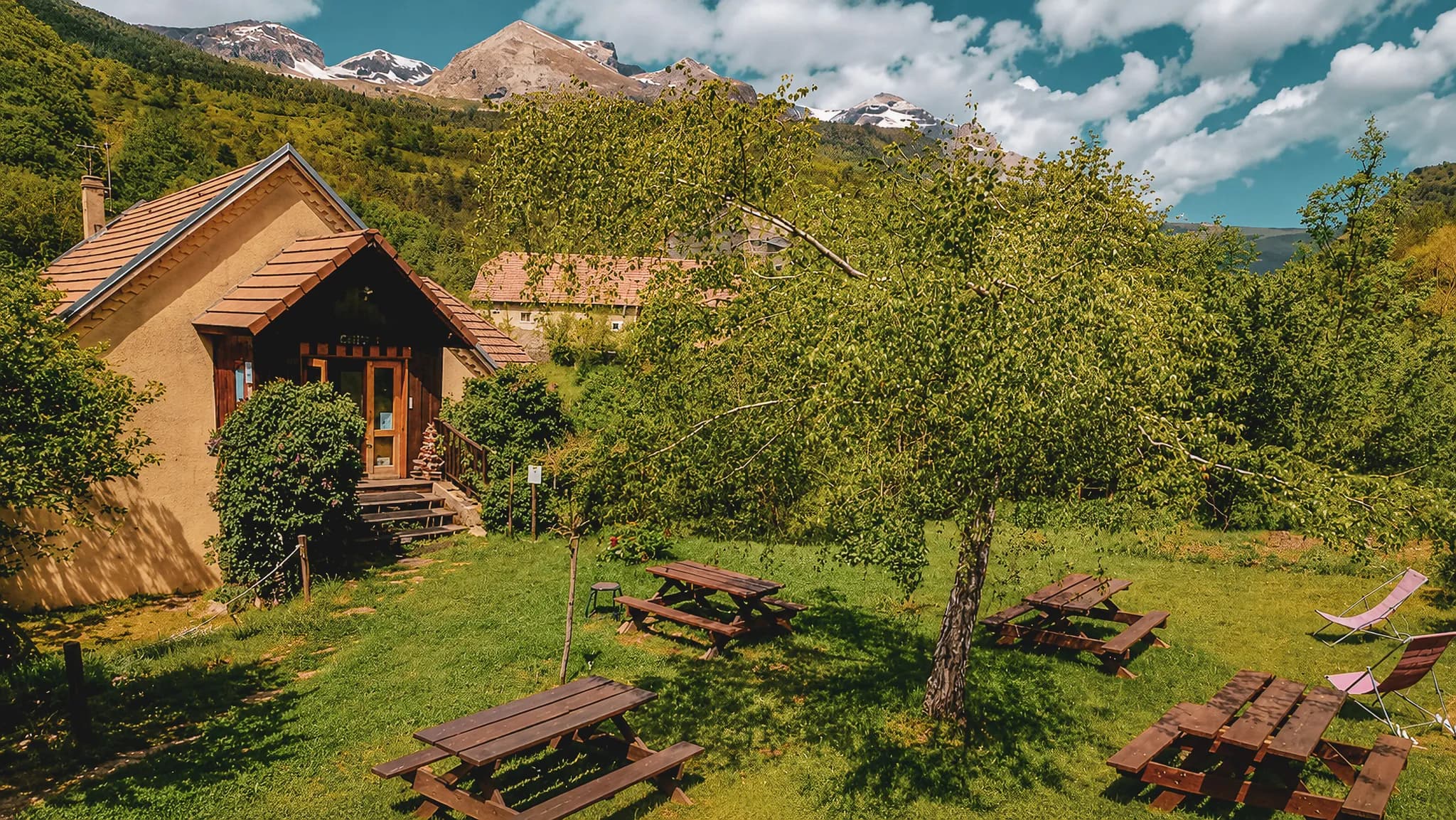 Charmante houten hut omgeven door groen, met majestueuze bergen op de achtergrond.