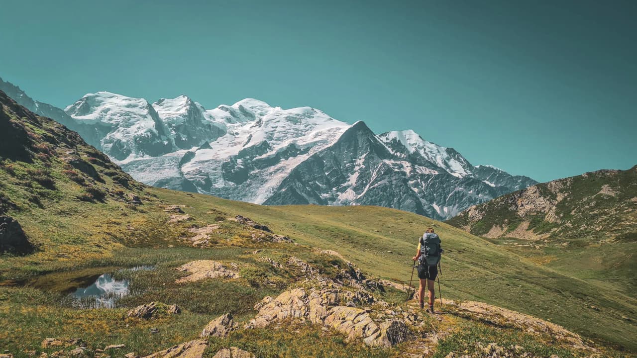 A hiker admiring the majestic snow-capped mountains in a lush green landscape.