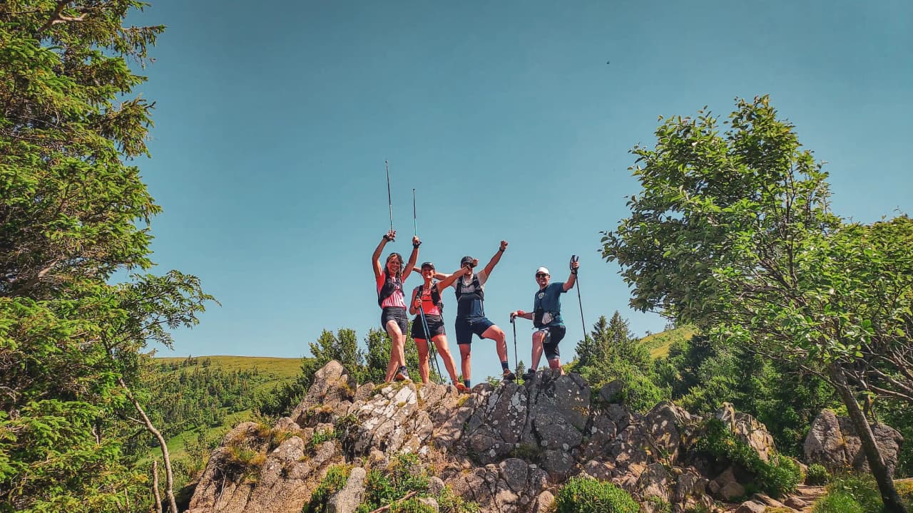 Quatre randonneurs jubilent sur un rocher avec vue sur les Vosges, sous un ciel bleu éclatant.